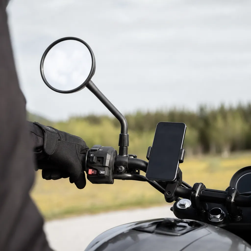 En mobiltelefon monterad på ett motorcykelstyre med förarens handskklädda hand intill